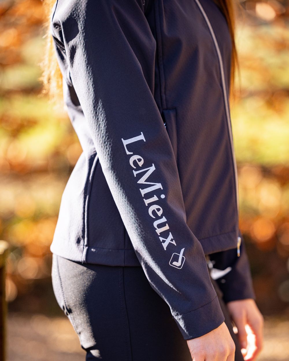 Navy coloured LeMieux Young Rider Elite Soft Shell Jacket with trees in background 