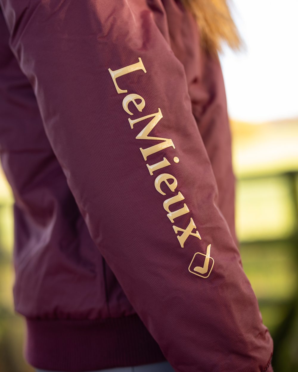 Burgundy coloured LeMieux Young Rider Elite Team Jacket on blurry field background 