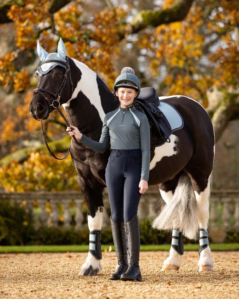 Petrol Coloured LeMieux Young Rider Mia Mesh Base Layer On A Yard Background