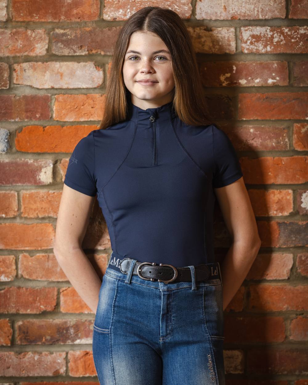 Indigo coloured LeMieux Young Rider Short Sleeve Base Layer on brick background
