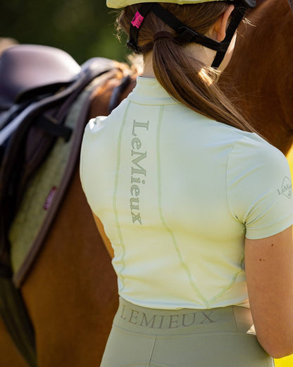 Pistachio coloured LeMieux Young Rider Short Sleeve Base Layer with horse in background 