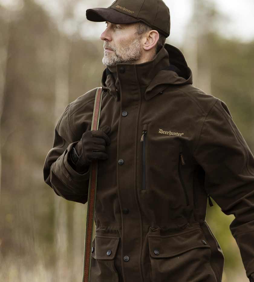 Men's shooting jackets \ Man wears Gamekeeper pro hunting jacket in dark green with peaked cap and shouldered rifle.