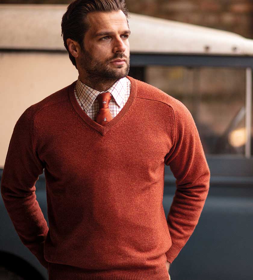 Man wearing Alan Paine v- neck knitted wool sweater in tiger orange colour, over tattersall shirt and tie.
