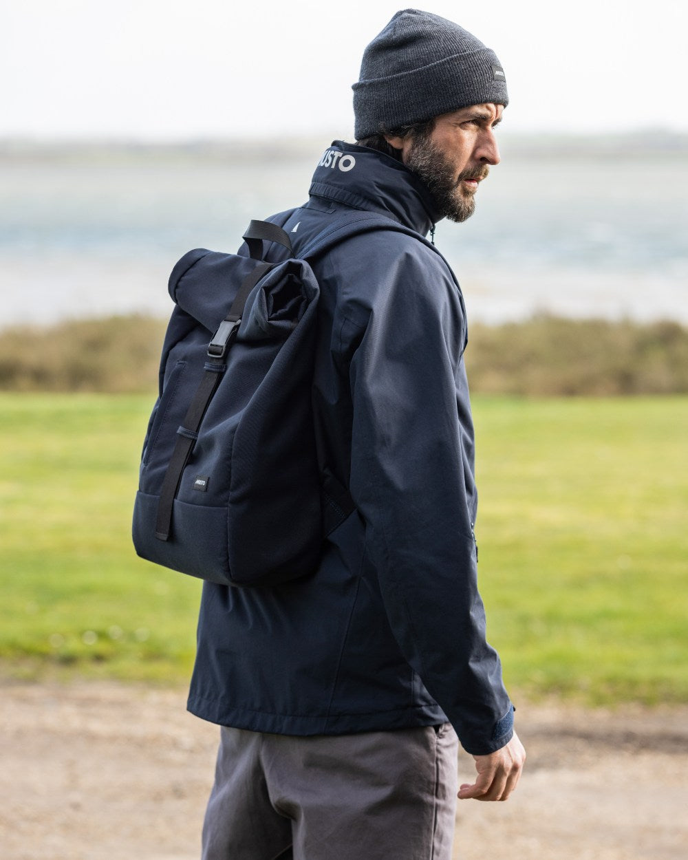 Navy Coloured Musto Canvas Roll Top Bag On A Coastal Background