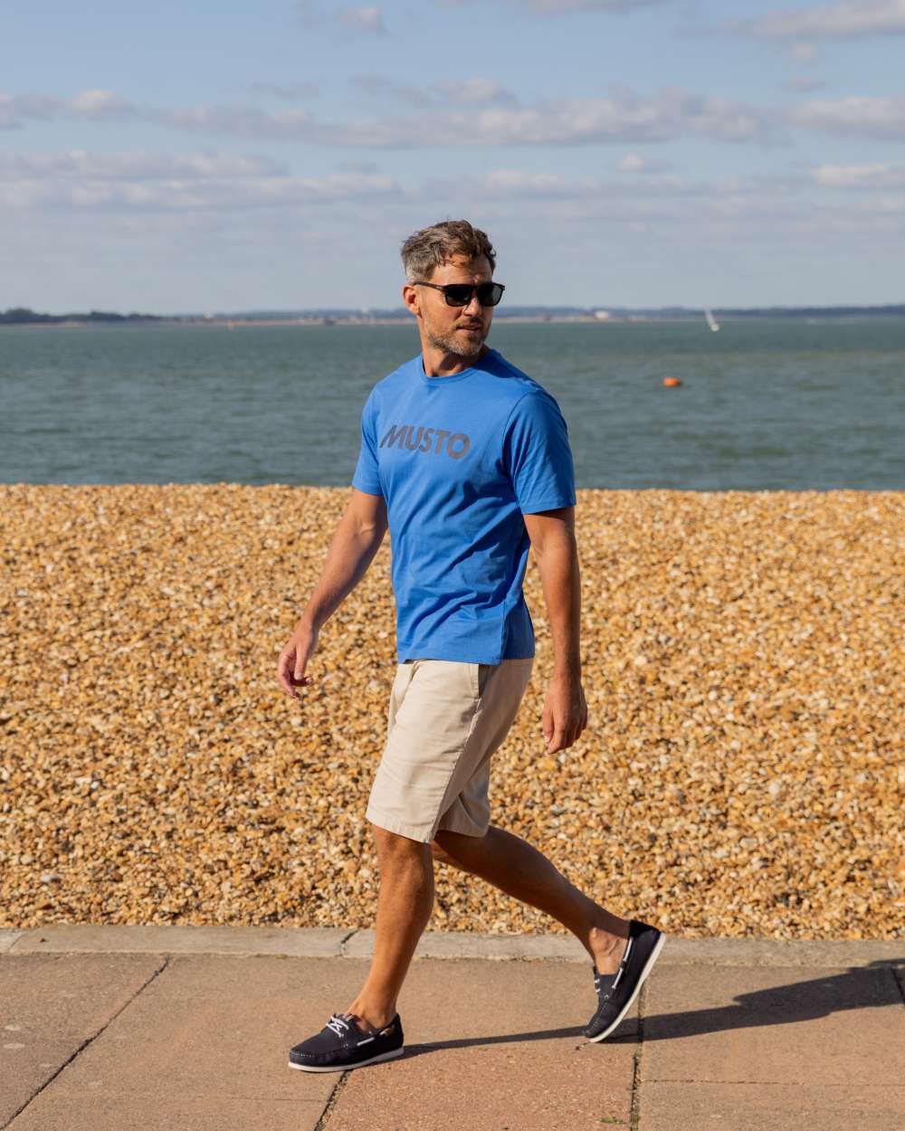 Nebulas Blue Coloured Musto Logo Cotton Tee on Beach Background