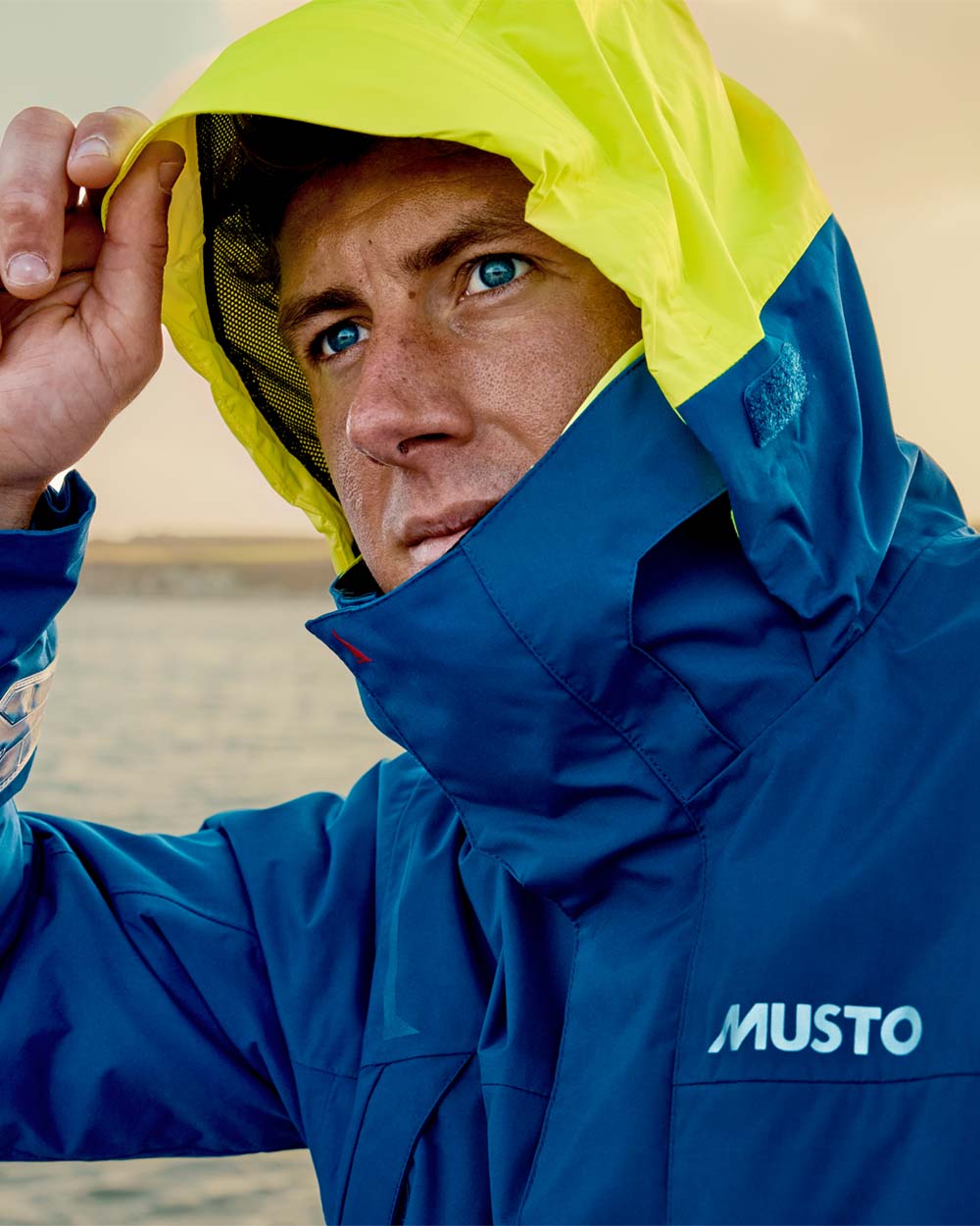 Racer Blue coloured Musto Mens BR1 Channel Jacket on Blurry Water background 