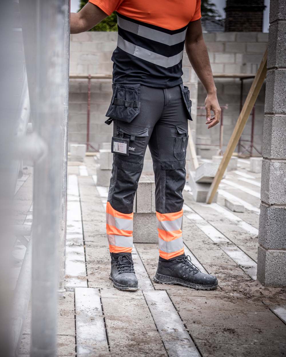 Black Orange Coloured Regatta Mens Hi-Vis X-Pro Stretch Holster Trousers Class 1 on Construction Site Background