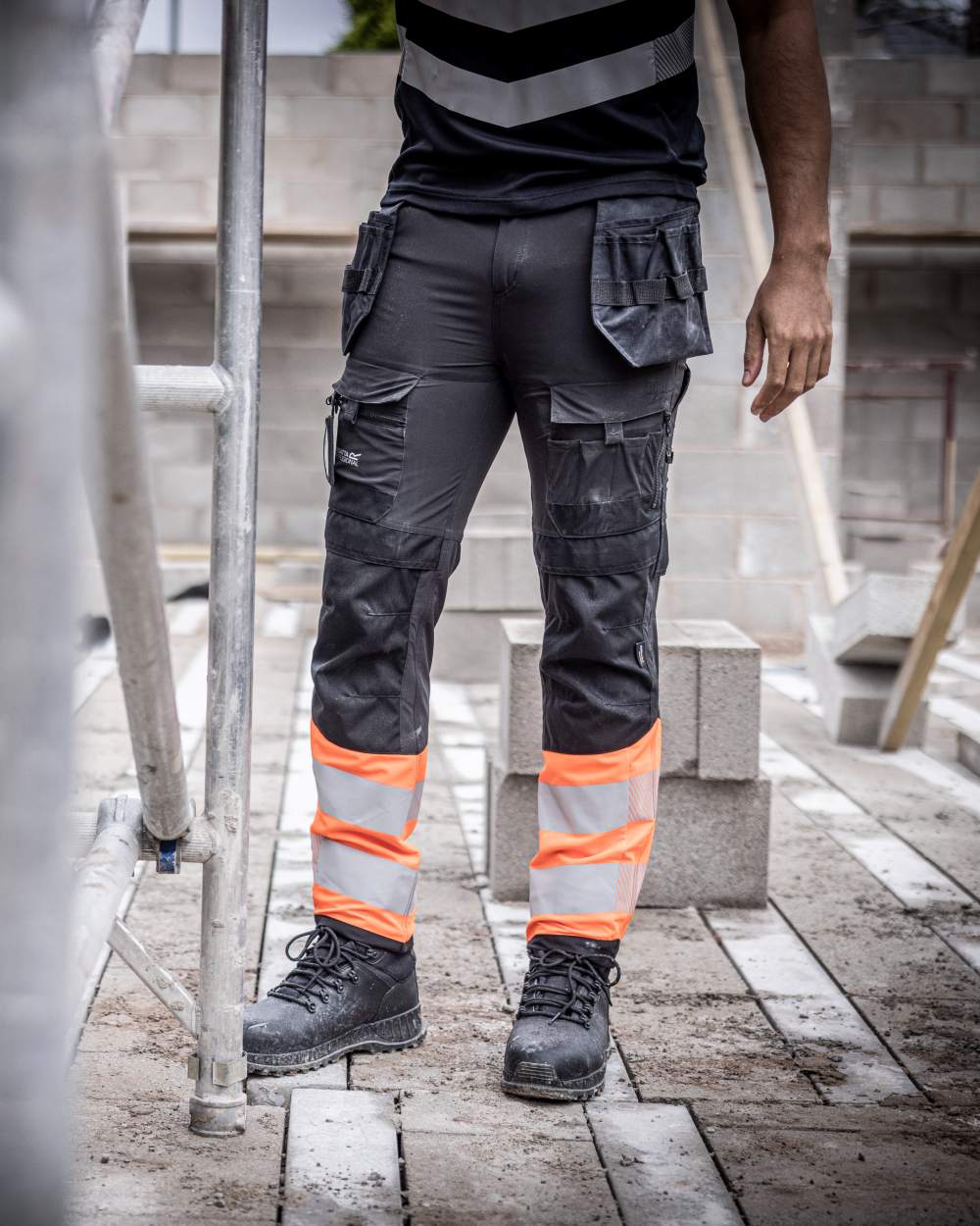 Black Orange Coloured Regatta Mens Hi-Vis X-Pro Stretch Holster Trousers Class 1 on Construction Site Background