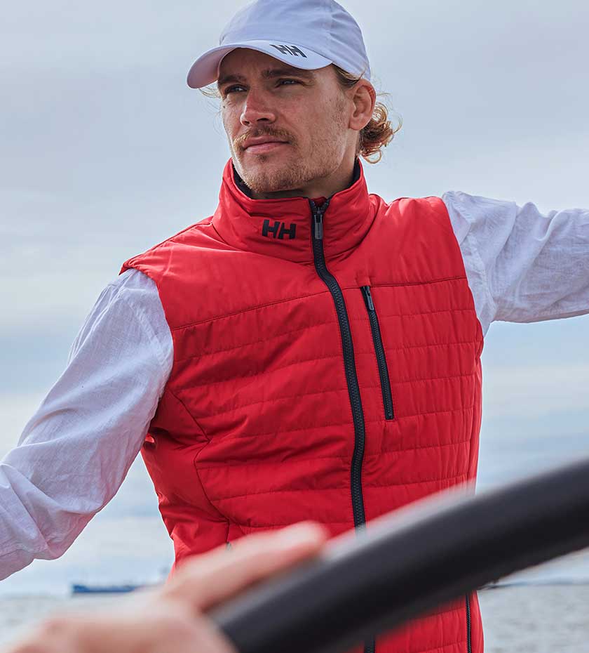 Sailing Gilets - man wears a red Helly Hansen quilted gilet and white hat with the sea in the background.