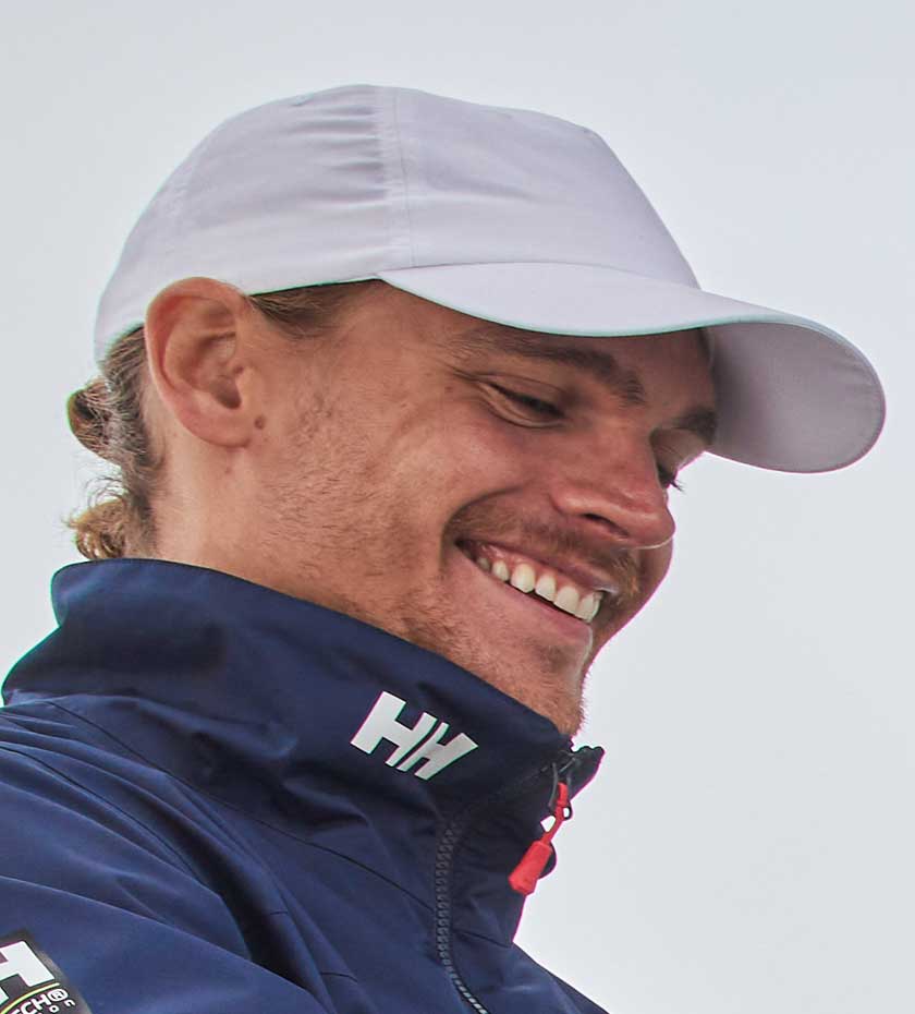 Sailing Hats - Close up of face of  a Man wearing a white peaked baseball cap and navy blue Helly Hansen Sailing jacket.
