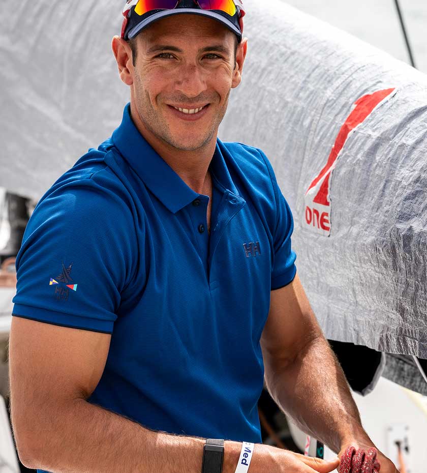Sailing Polo shirts Man wears a bright blue Helly Hansen Polo shirt with a yacht sail in the background.