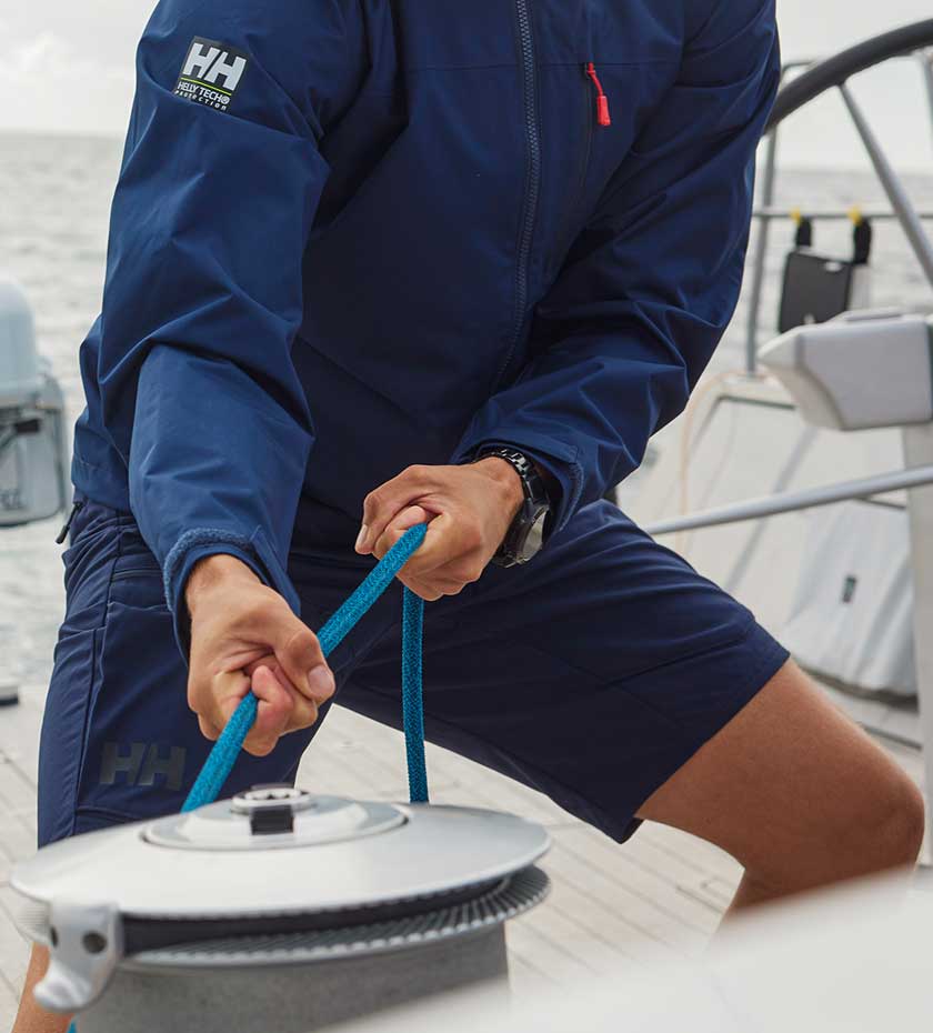 A man wearing Navy coloured technical sailing shorts works a winch on an ocean going yacht.
