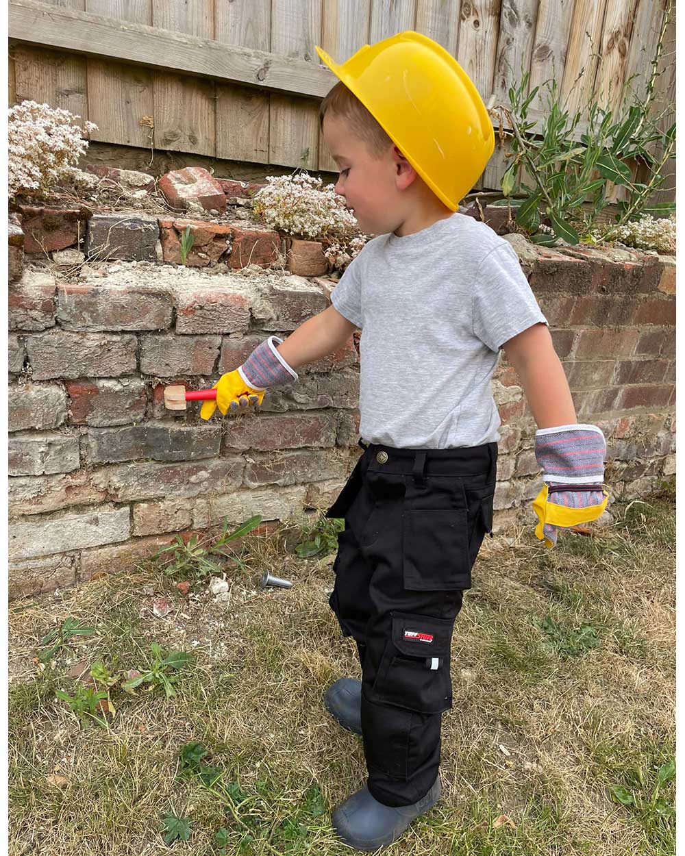 Small boy in yellow safety hat wearing TuffStuff Junior Pro Work Trousers in Black 