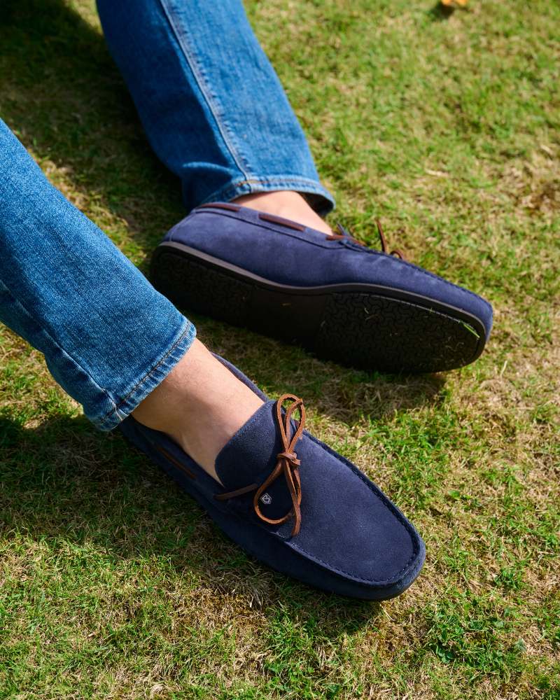 Pair of navy suede Dubarry deck shoes with brown bow laces being worn on green grass. 