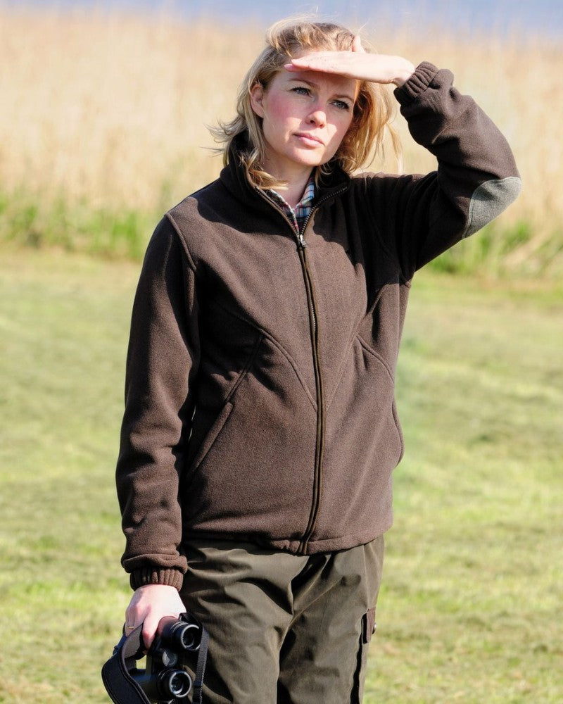 Female model stood in a field wearing a brown Laksen fleece, looking into the sun with one hand up and binoculars in the other. 