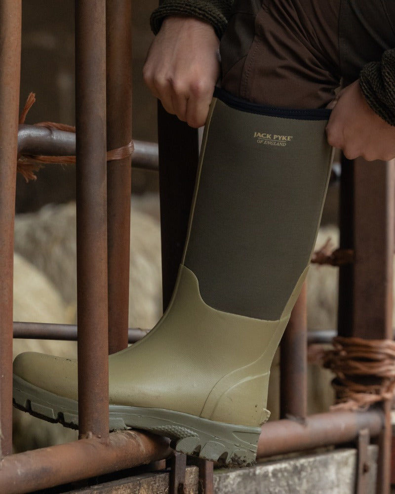 Green rubber and neoprene Jack Pyke wellingtons being worn on a rusted metal farm bar. 