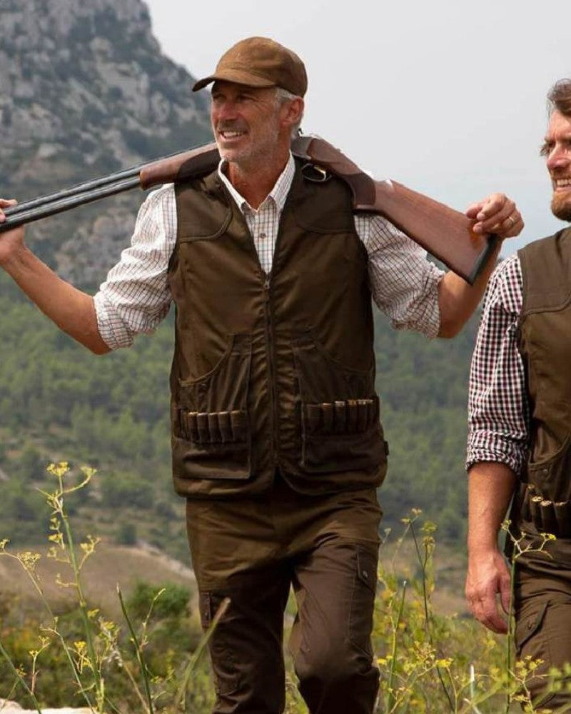 Man wearing a Percussion shooting gilet while carrying a shotgun outdoors in the countryside