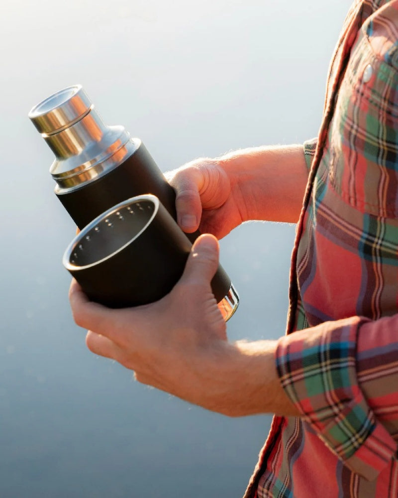 Person holding a Klean Kanteen insulated flask and cup outdoors