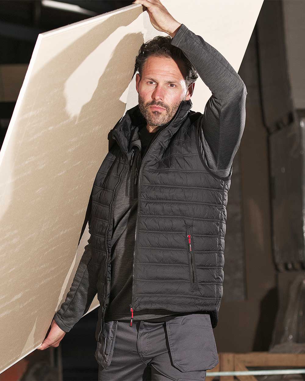 Construction worker carrying plasterboard wearing TuffStuff Elite Quilted Bodywarmer in black