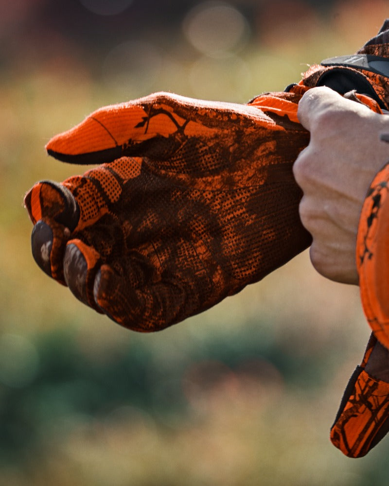 Close up of orange camo Harkila gloves being put onto the models hand. 