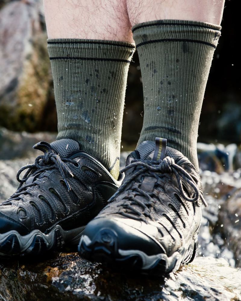 Pair of green Bridgedale socks being worn in a pair of walking boots while stood on a rock. 
