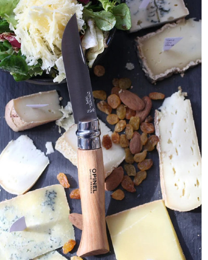 Opinel folding knife with wooden handle displayed alongside cheeses and picnic food