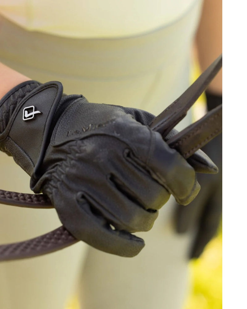 Person wearing black LeMieux riding gloves while holding horse reins