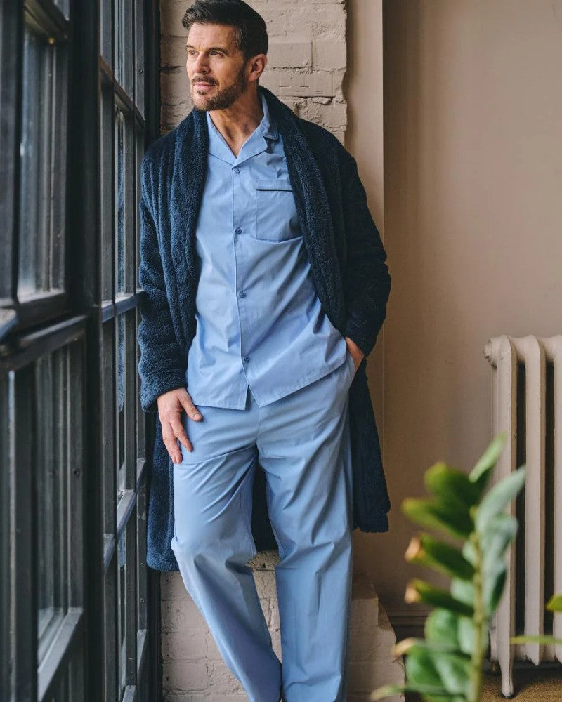 Man wearing HJ Hall blue nightwear and navy dressing gown indoors beside a window