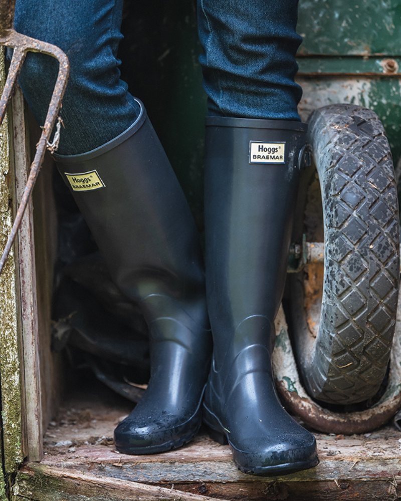 Navy Hoggs of Fife wellingtons stood in a wooden doorway next to a wheelbarrow. 