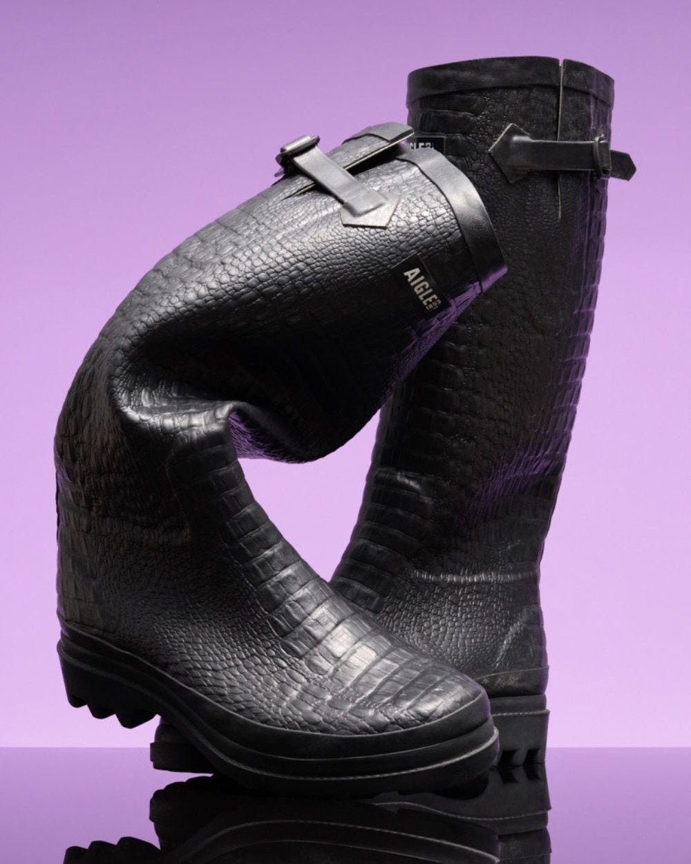 Noir coloured Aigle Womens Aiglentine 2 Crocodile Style Wellingtons on lilac background 