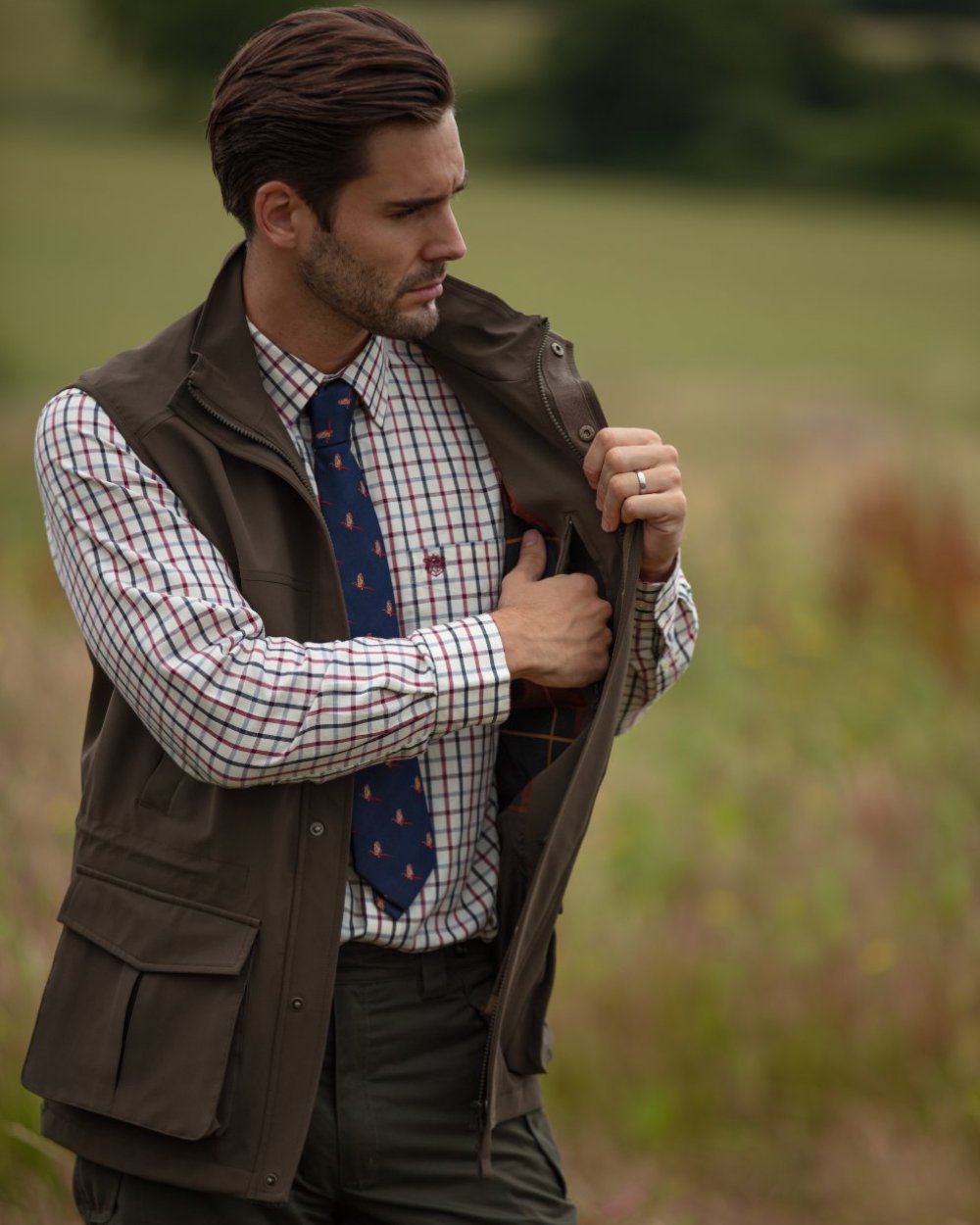 Olive coloured Alan Paine Lockwood Mens Shooting Waistcoat on blurry field background 