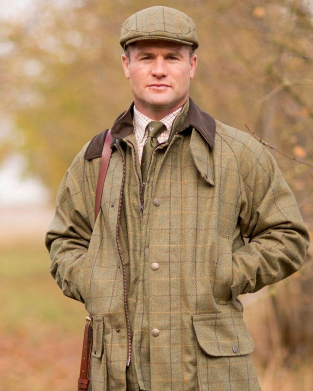 Dark Moss coloured Alan Paine Rutland Waterproof Tweed Shooting Coat on forest background 