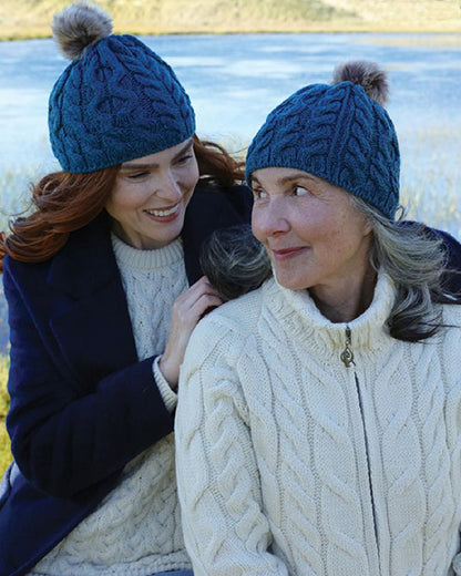 Teal Coloured Aran Knitted Faux Fur Bobble Hat on lake background 