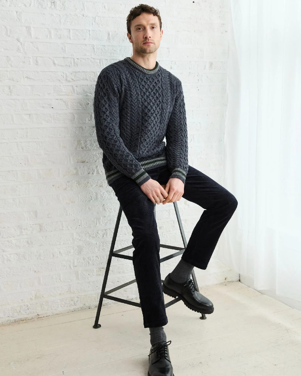 Dark Grey Coloured Aran Mens Inishbeg Stripe Crewneck Merino Sweater on indoor background 