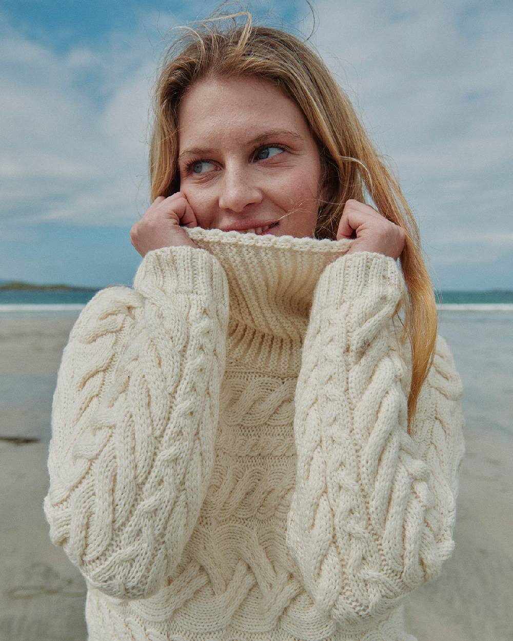 Cream Coloured Aran Womens Derreen Horizontal Cable Sweater on outdoor background 