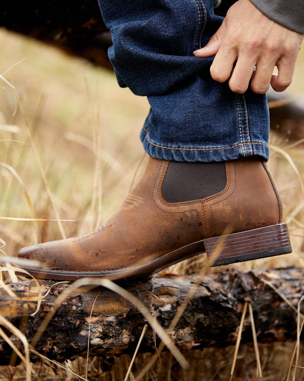 Oily Distressed Tan Coloured Ariat Mens Booker Ultra Square Toe Western Boot on dry grass background 