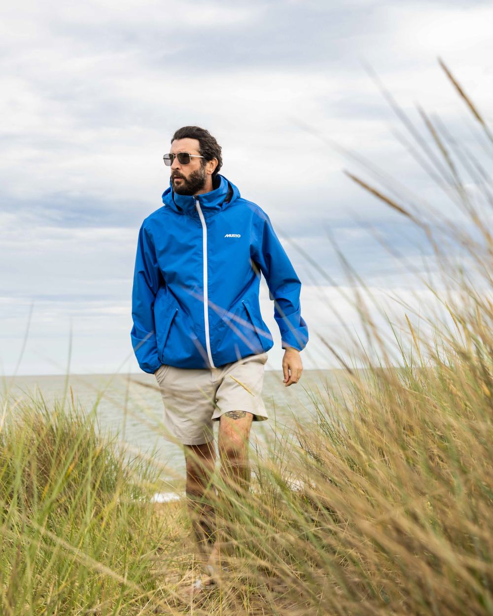 Aruba Blue Coloured Musto Mens Nautic Rain Jacket On A Beach Background 