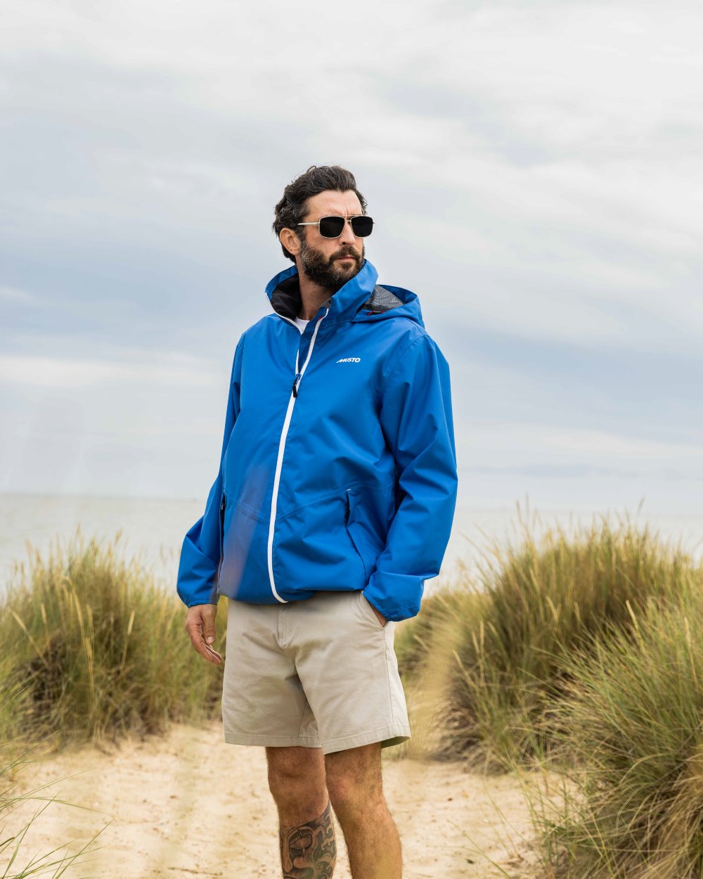 Aruba Blue Coloured Musto Mens Nautic Rain Jacket On A Beach Background 