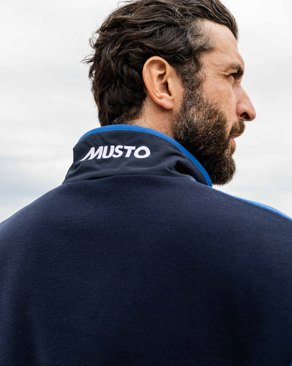 Aruba Blue/Navy Coloured Musto 64 Fleece Pullover On A Coastal Background 