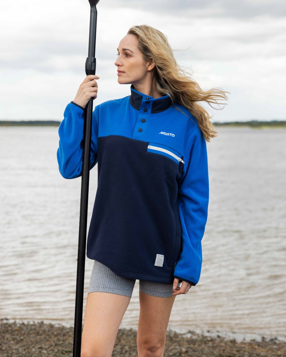 Aruba Blue/Navy Coloured Musto 64 Fleece Pullover On A Coastal Background 