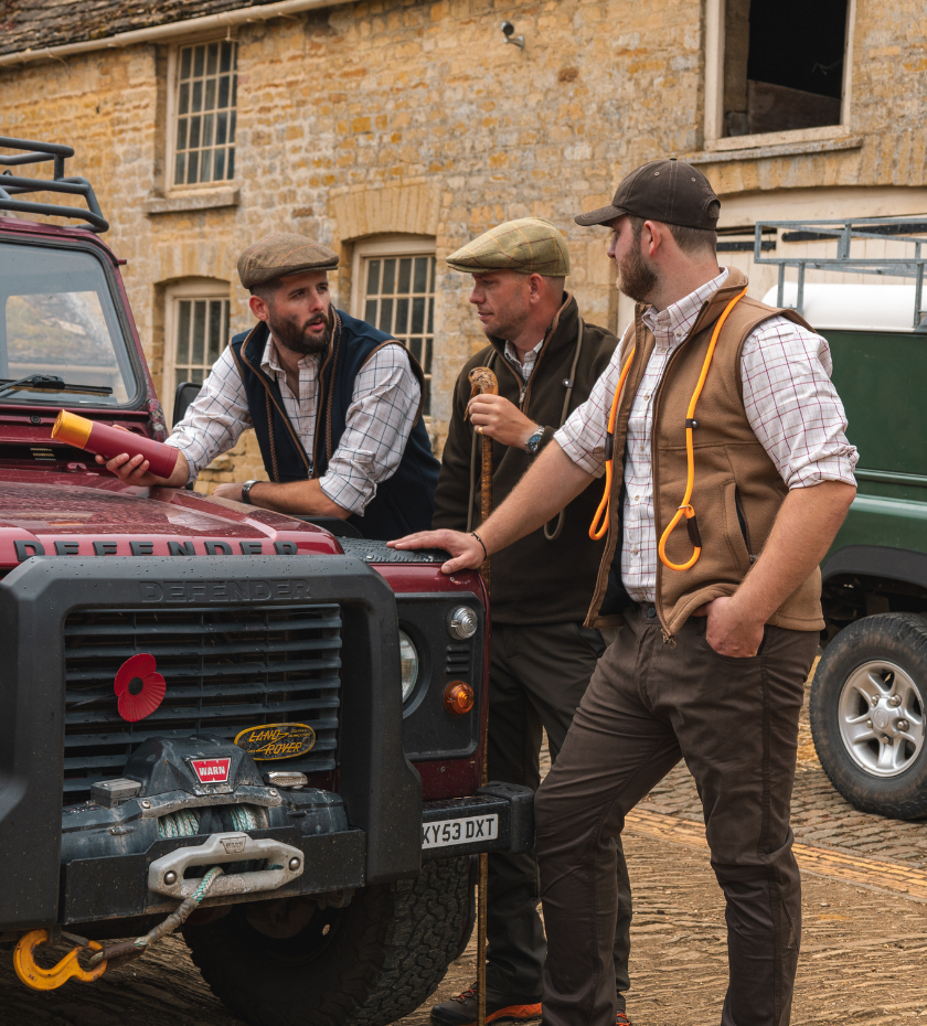 Three men in traditional country shooting clothing standing beside a Land Rover during a beating day
