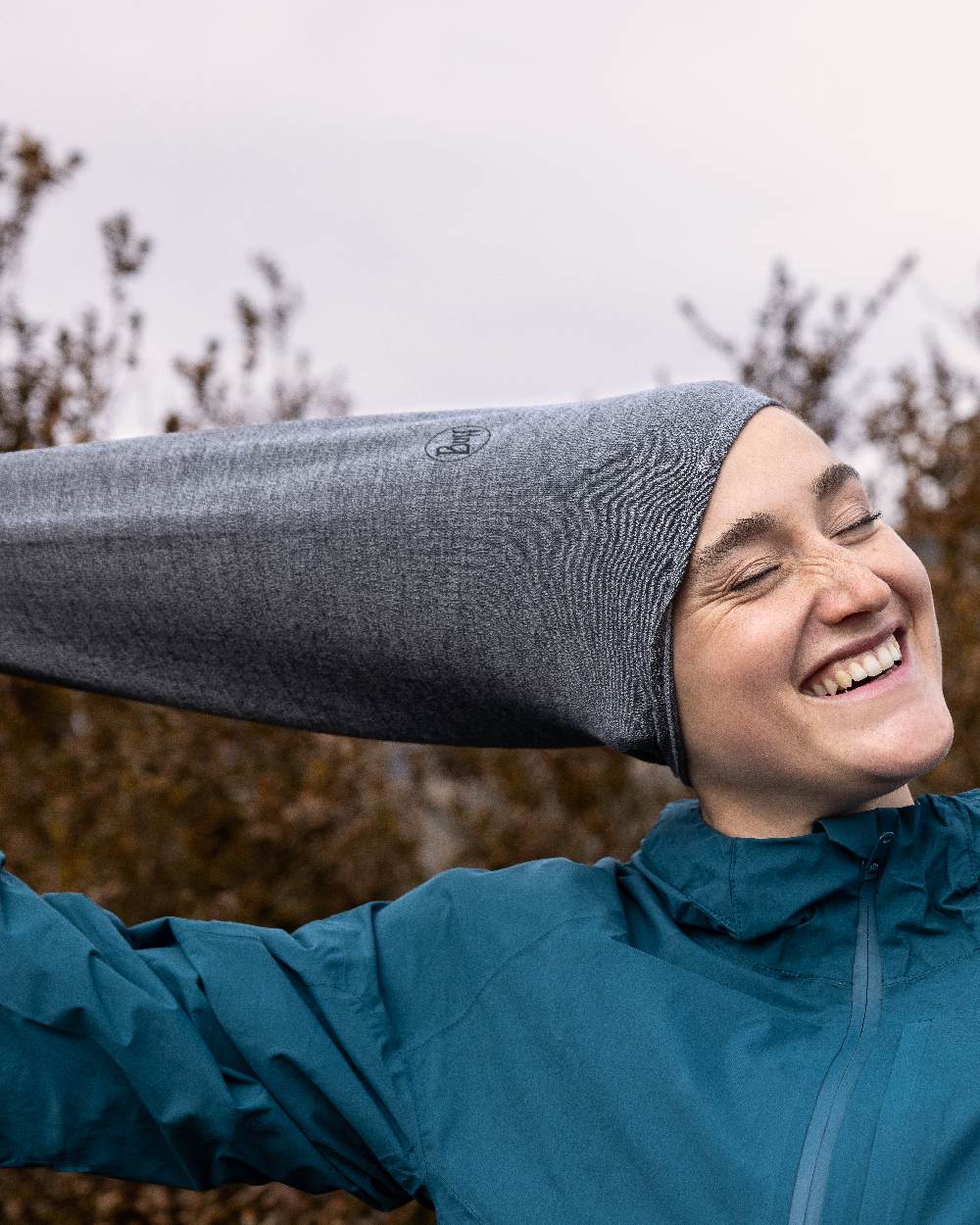 Light Grey Coloured Buff Merino Lightweight Neck Warmer on forest background 