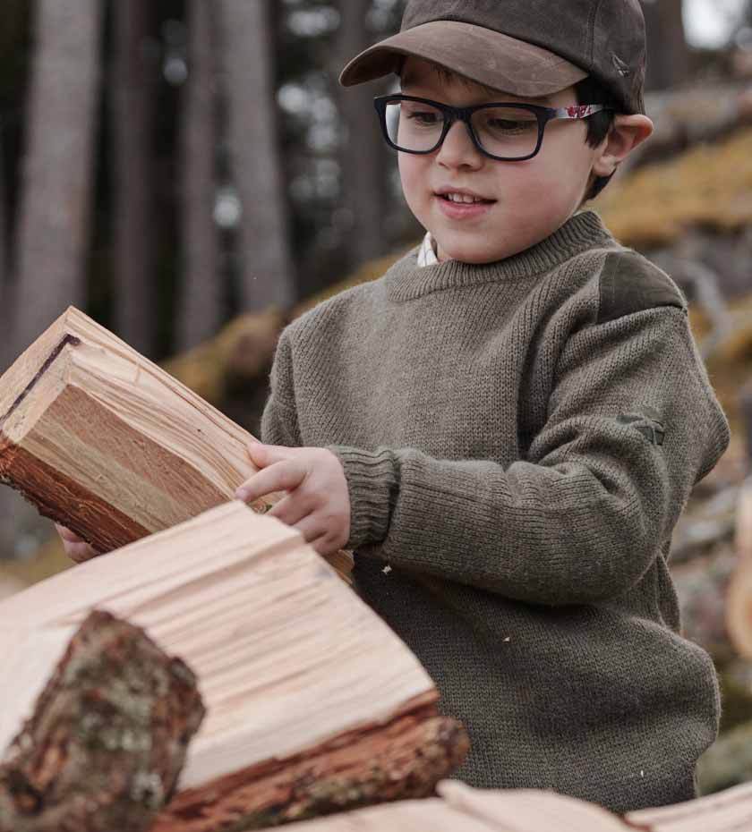 Hoggs of Fife Children's clothing. Small boy in sweater lifts a log.