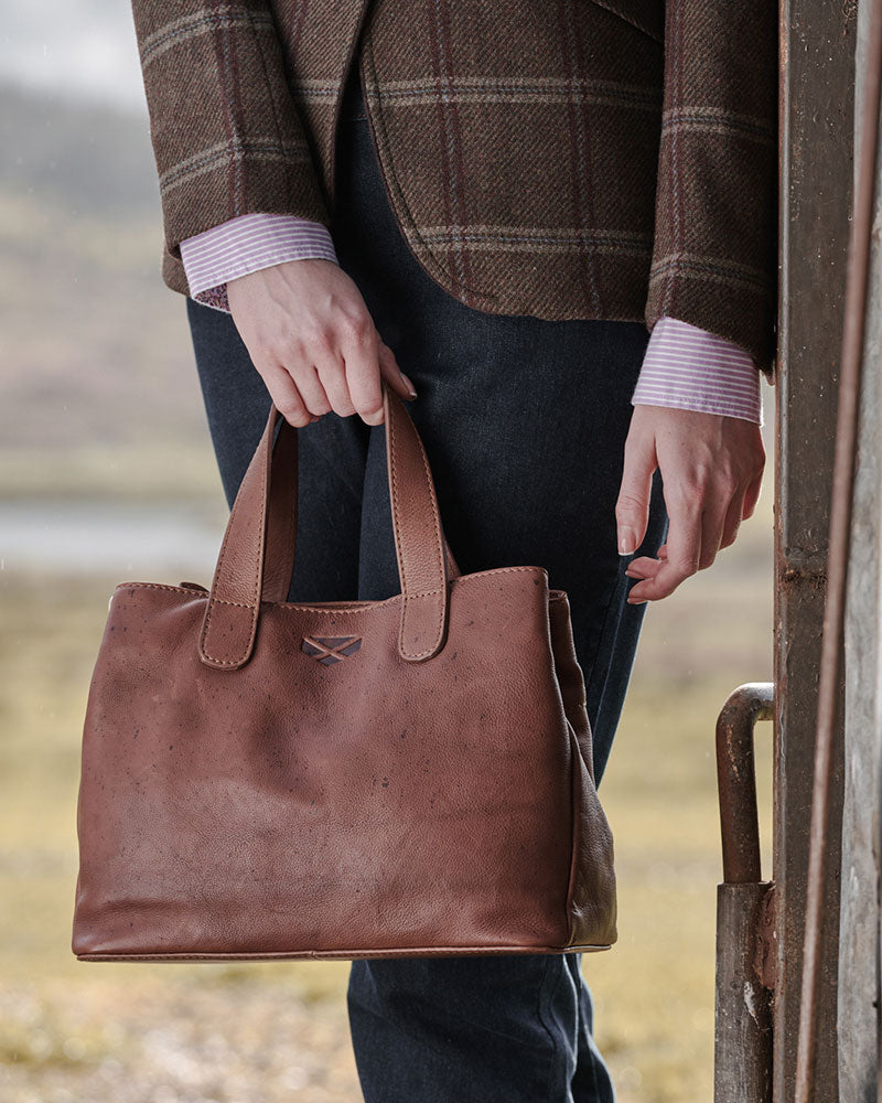 Female model holding a Hoggs of Fife handbag n a blurred natural background