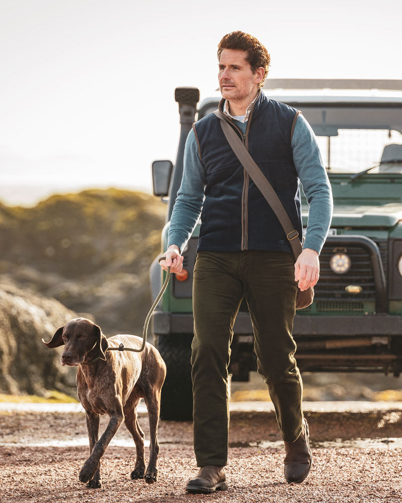 Male model wearing a Hoggs of Fife gilet and walking a dog n a blurred natural background