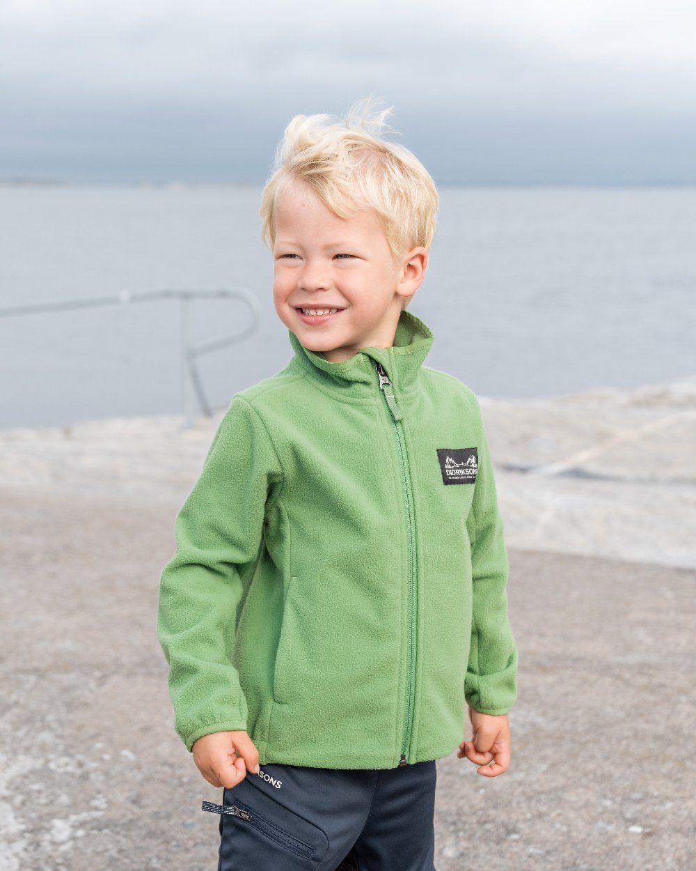 Algae Green coloured Didriksons Childrens Muskot Jacket on blurry background 