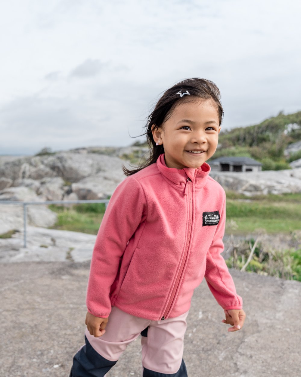 Dusty Azalea coloured Didriksons Childrens Muskot Jacket on coastal background 
