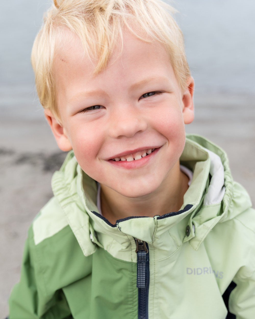 Light Algae Green coloured Didriksons Childrens Pilvi Jacket on blurry background 