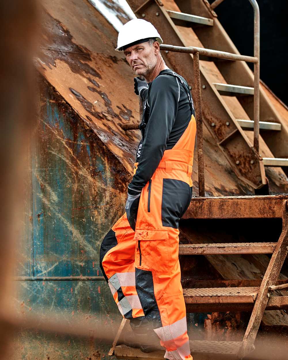 Fluorescent Orange Black Coloured Elka Mens Visible Xtreme Stretch Combi Trousers on construction background 