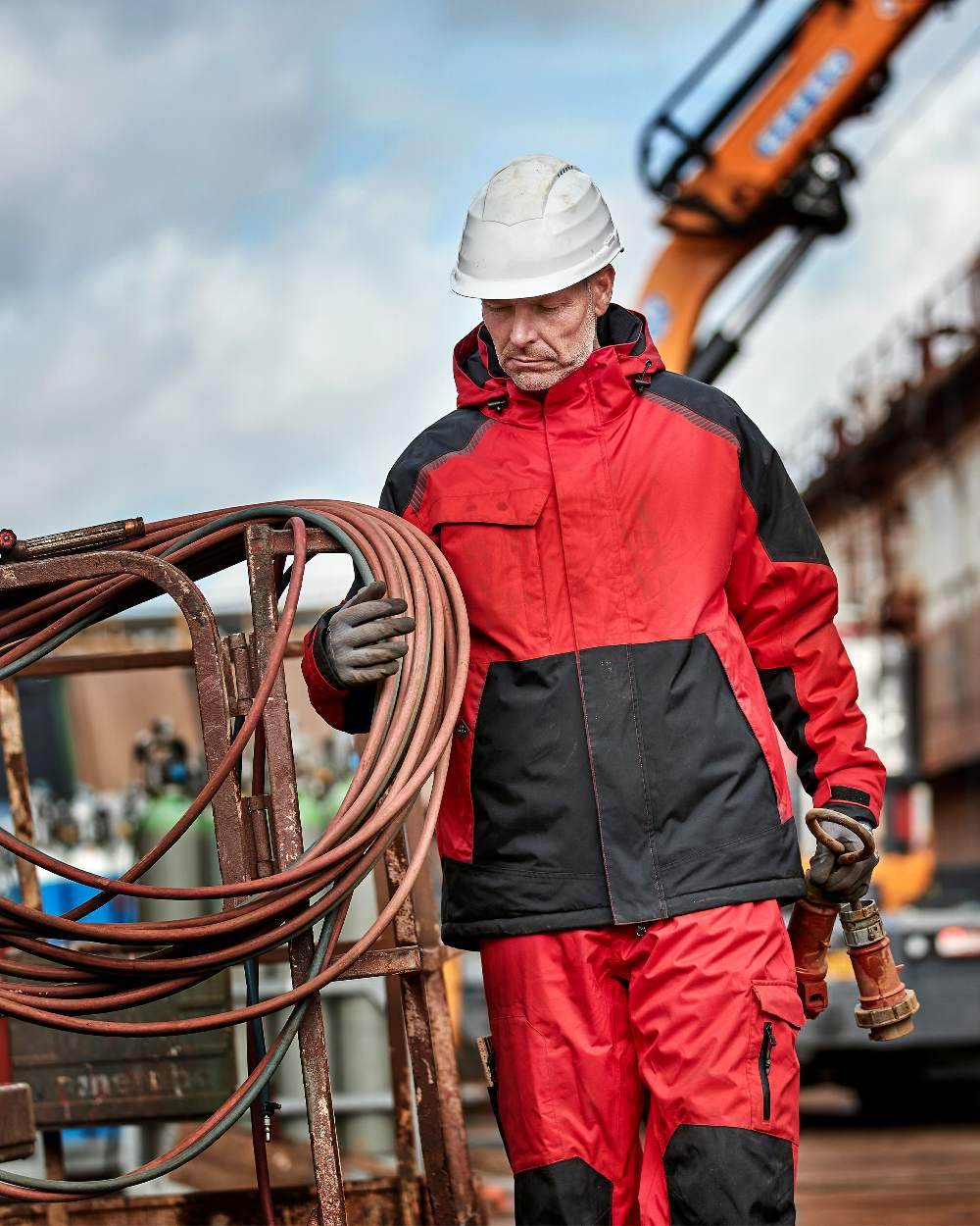 Red Black Coloured Elka Mens Working Xtreme Stretch Waist Trousers on construction background 